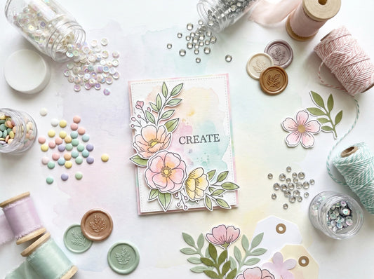 Paper crafting embellishments including sequins, enamel dots, gems, ribbon, wax seals, and die-cuts around a handmade card.