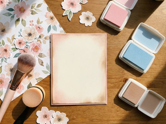 Cardmaking workspace with a softly ink-blended card panel, digital paper scrap, ink pads, and blending tools on a wooden desk.