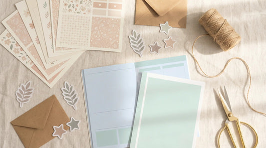 Flat lay of pastel printable planner pages, stickers, kraft envelopes, twine and gold scissors on fabric, styled like a small Etsy printable shop workspace.