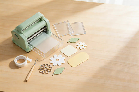Manual die-cutting machine with pastel cardstock die-cuts, metal dies, and cutting plates on a craft table.