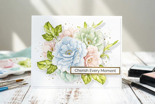 Handmade floral greeting card with layered pastel blooms and greenery, featuring the sentiment “Cherish Every Moment” on a white rustic craft table.